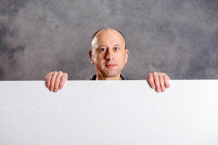 young man with a white advertising board in front of gray backgroundの写真素材