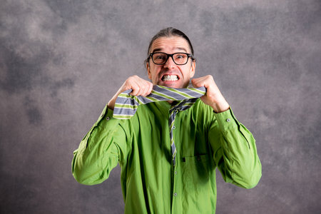 stressed man in green shirt and glasses showing his teeth and necktie and looking crazy in to the cameraの写真素材