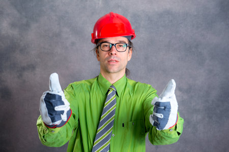 young architect in green shirt with red helmet and thumb upの写真素材