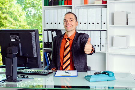 young business man at his desk with thumb upの写真素材