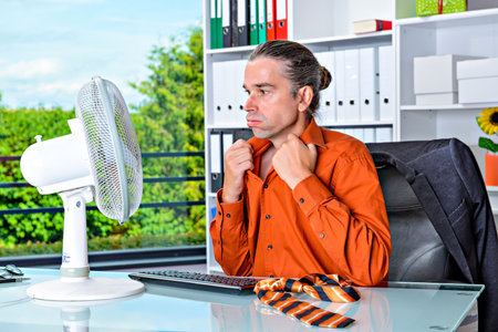 business man with ventilator at his desk in summerly hot officeの写真素材