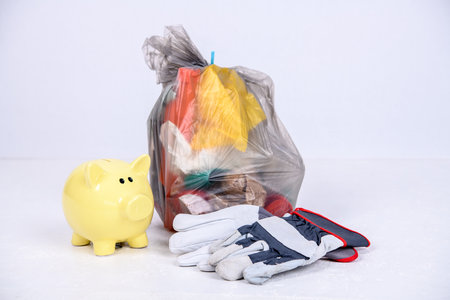 garbage bag with defferent content with yellow piggy bank and work glovesの写真素材