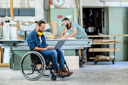 disabled worker in wheelchair in a carpenter's workshop with his colleagueの写真素材