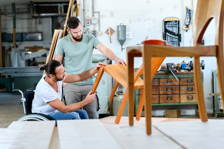 disabled worker in wheelchair in a carpenter's workshop with his colleagueの写真素材