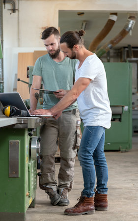 two worker in a carpenter's workshop with clipboard and computerの写真素材