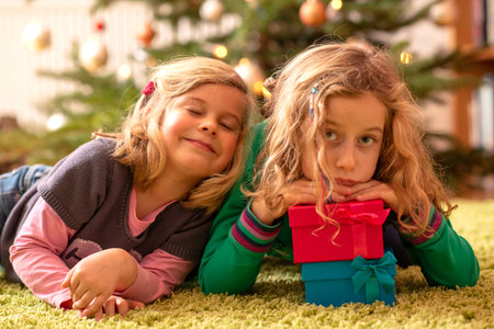two blond girls with presents in front of christmas treeの写真素材