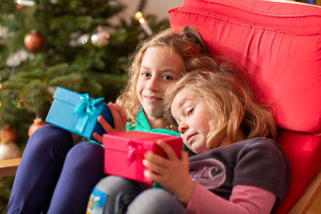 two blond girls with presents in front of christmas treeの写真素材