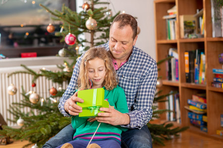 father and daughter together on sled in fron tof christmas treeの写真素材