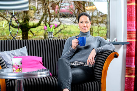 young dark haired woman at home with cup of coffeee relaxingの写真素材