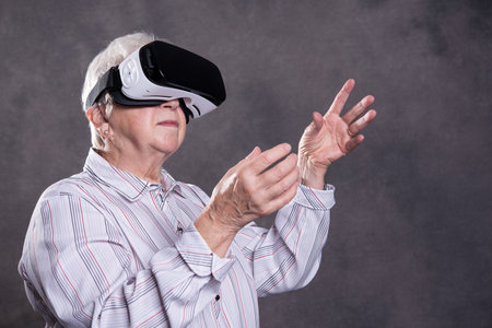 gray hairy elderly woman using virtual reality glasses and looking surprisedの写真素材