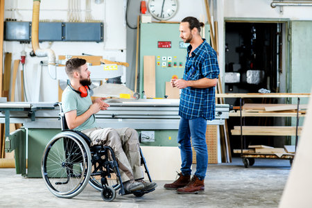 disabled worker in wheelchair in a carpenter's workshop with his colleague in conversationの写真素材