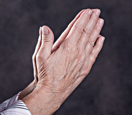wrinkly hands of  elderly woman praying in front of dark backgroundの写真素材