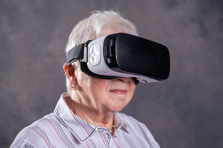 gray hairy elderly woman using virtual reality glasses and looking surprisedの写真素材