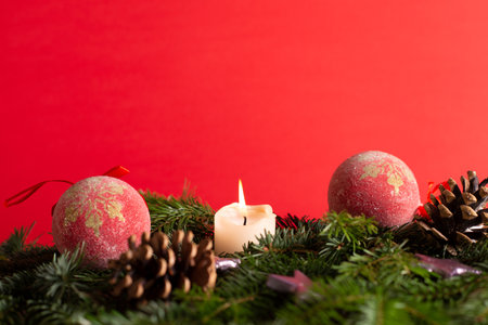 christmas decor with tree-balls, candle, branch and cone in front of red backgroundの写真素材