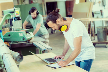 worker in a carpenter's workshop with clipboard and computer