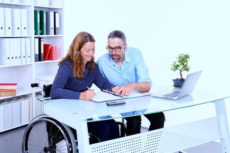 disabled businesswoman in wheelchair and her colleague in the officeの写真素材