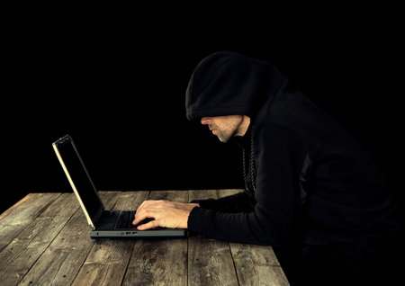 hacker in black hoody with laptop  in front of black backgroundの写真素材