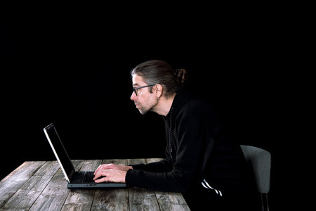 man in black hoody with laptop  in front of black backgroundの写真素材