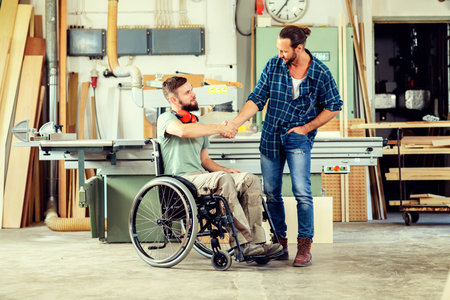 disabled worker in wheelchair in a carpenter's workshop with his colleague in conversationの写真素材