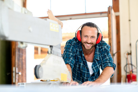 young worker working with saw in a carpenter's workshop and smilingの写真素材