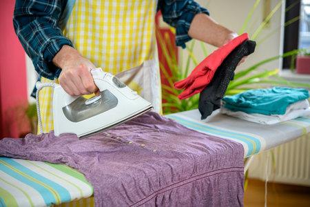 man with iron on ironing board with clothers in living roomの写真素材