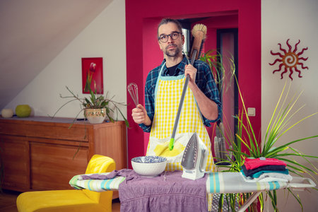 man with iron,broom, bowl and whisk in living roomの写真素材