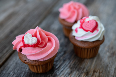pink and white muffins on wooden ground with heart and whipping creamの写真素材