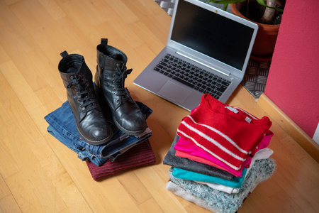 pile of second hand clothing and  shoes with computer on floor in living roomの写真素材