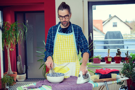 man with iron, bowl and whisk in living roomの写真素材