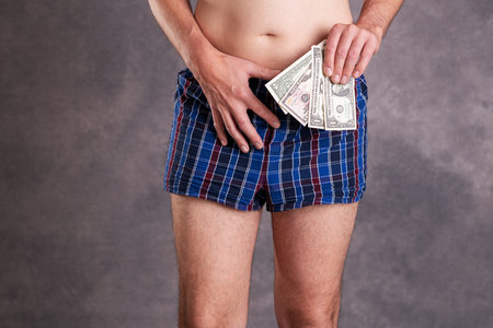 man in blue plaid boxer shorts with money in front of gray backgroundの写真素材