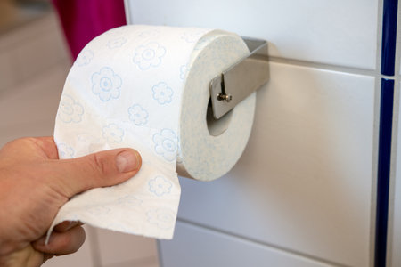 hand taking white toilet paper on wall with white tilesの写真素材