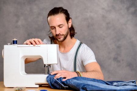 young tailor with sewing machine in front of gray backgroundの写真素材