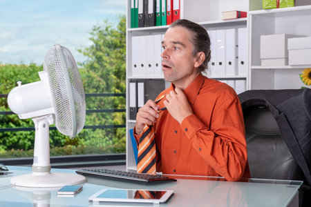 business man with ventilator at his desk in summerly hot officeの写真素材