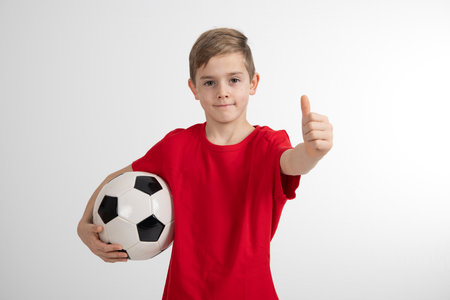 boy in red shirt with soccer ball and thumb up in front of white backgroundの写真素材