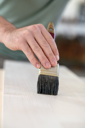 worker in a carpenter's workshop painting wood with brushの写真素材