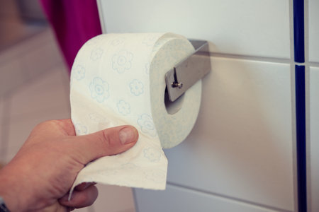hand taking white toilet paper on wall with white tilesの写真素材