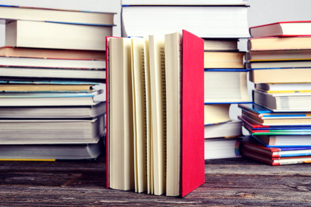 one book in front of piles of different books on wooden tableの写真素材