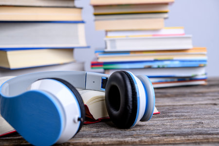 book with headphone in front of piles of different books on wooden tableの写真素材
