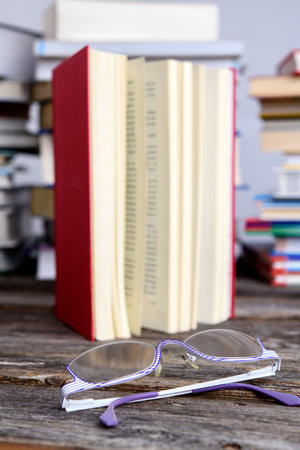 book and reading glasses in front of piles of different books on wooden tableの写真素材
