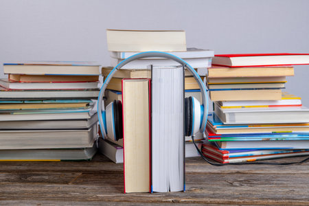 book with headphone in front of piles of different books on wooden tableの写真素材