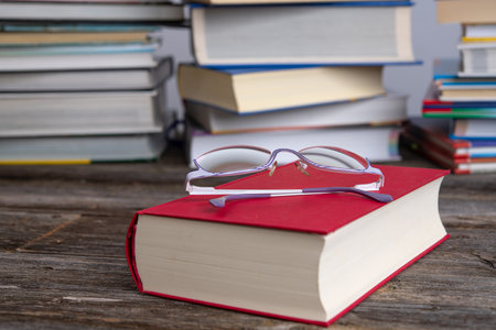 book and reading glasses in front of piles of different books on wooden tableの写真素材