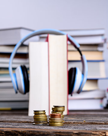 book with headphone in front of piles of different books on wooden tableの写真素材