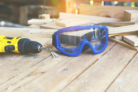 Wireless electric drill with screw and blue eye mask protection on wooden table,diy at home concept.の写真素材