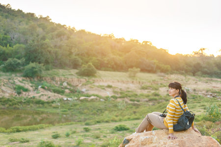 Young Woman in yellow sweaters sitting on a giant rock for rest and watching sunset between travel in mountain for her vacation.の写真素材