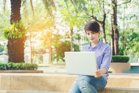Beautiful short hair woman sitting on the floor and using laptop for outdoor working her business in the park.のeditorial素材