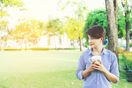 Beautiful short hair woman standing in the green yard and drinking a favorite beverage in white cup for resting between her outdoor working business in the park.の写真素材