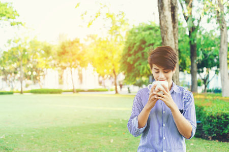 Beautiful short hair woman standing in the green yard and drinking a favorite beverage in white cup for resting between her outdoor working business in the park.の写真素材