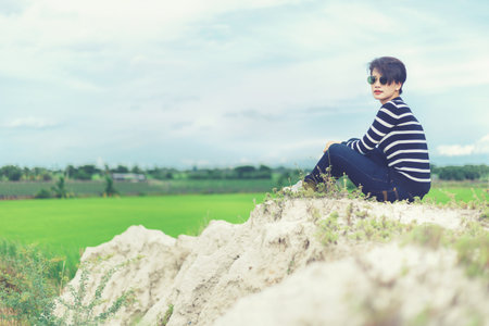 Beautiful woman in black and white sweater siting on sand mountain with rice field background.の写真素材