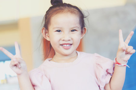 Happiness little girl look a camera and smiling for take a photo and show 2 fingers signの写真素材