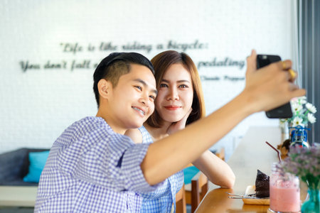 Homosexual lovers using a smart phone for take a selfie photo in a cafe.の写真素材